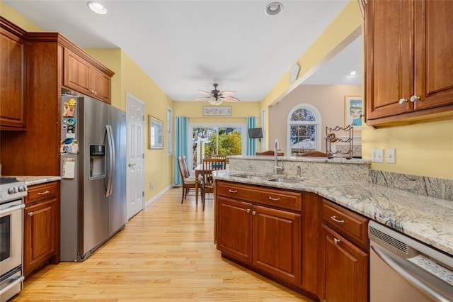 kitchen with light hardwood / wood-style floors, stainless steel appliances, sink, ceiling fan, and light stone countertops