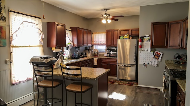 kitchen featuring a baseboard radiator, a kitchen bar, ceiling fan, stainless steel appliances, and dark hardwood / wood-style floors