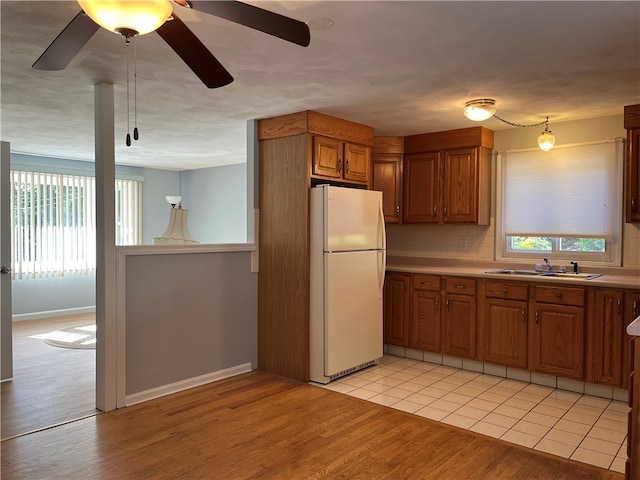 kitchen with decorative backsplash, hanging light fixtures, sink, white refrigerator, and light hardwood / wood-style floors