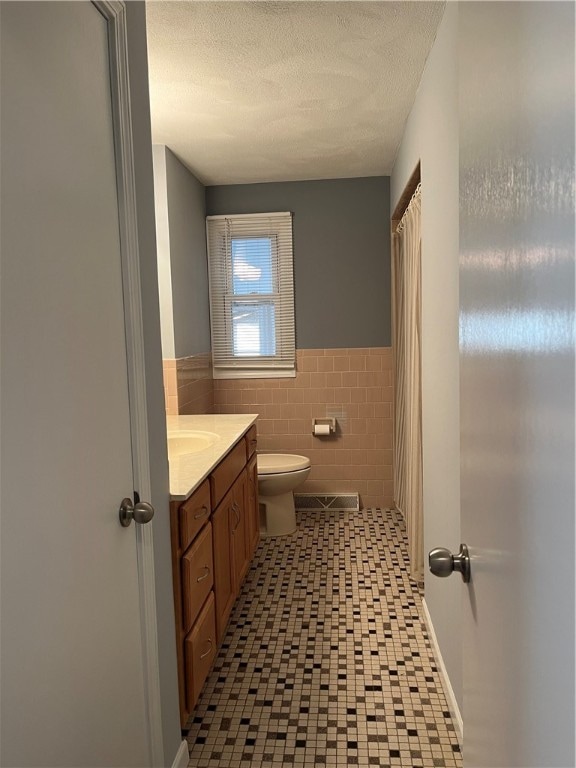 bathroom with tile walls, vanity, a textured ceiling, and toilet