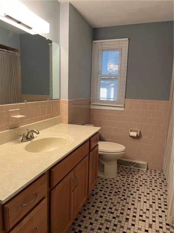 bathroom with vanity, toilet, tile walls, and tile patterned flooring