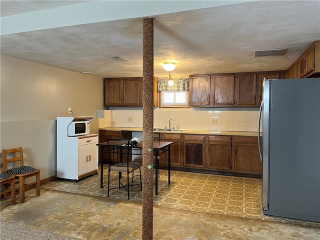 kitchen with tasteful backsplash, stainless steel refrigerator, sink, and a textured ceiling