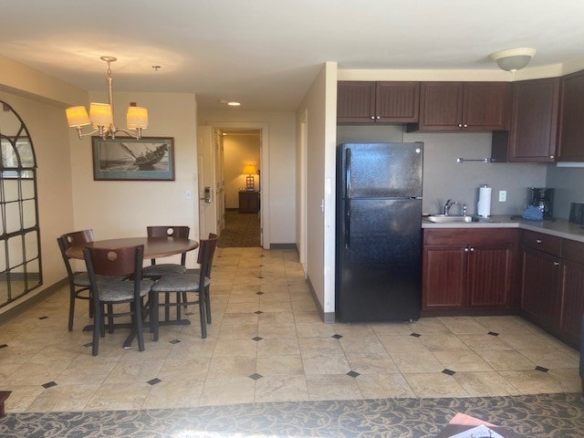 kitchen with a notable chandelier, pendant lighting, light tile patterned floors, and black fridge