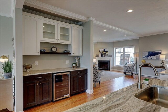 bar featuring sink, dark brown cabinetry, light wood-type flooring, beverage cooler, and white cabinetry