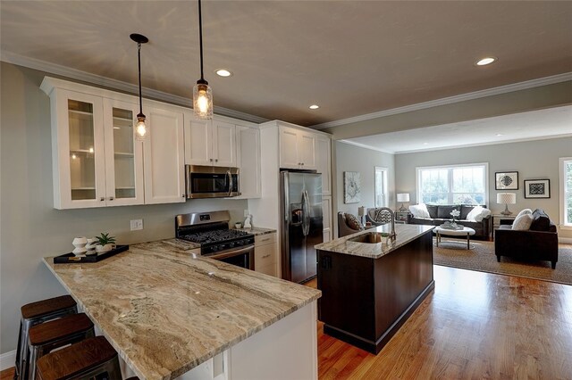 kitchen with a kitchen island, appliances with stainless steel finishes, white cabinetry, pendant lighting, and light hardwood / wood-style floors