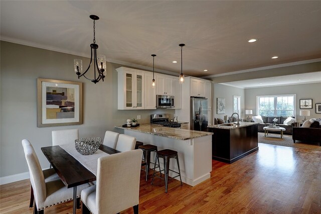 dining area with sink, crown molding, a chandelier, and light wood-type flooring