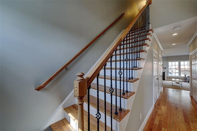 stairway with ornamental molding and hardwood / wood-style floors