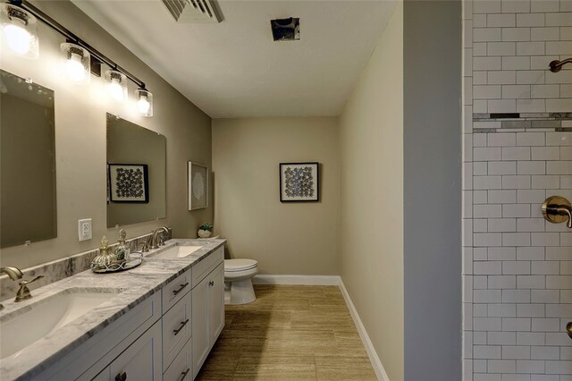 bathroom with toilet, vanity, a tile shower, and wood-type flooring