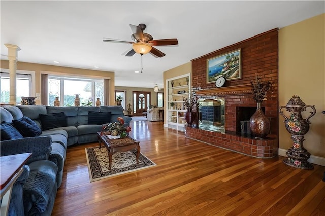 living room featuring hardwood / wood-style floors, a fireplace, built in features, and ceiling fan