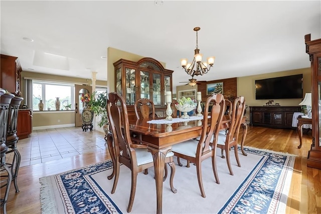 dining room featuring decorative columns, light hardwood / wood-style flooring, and ceiling fan with notable chandelier