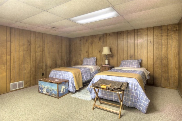 bedroom with carpet floors, wooden walls, and a drop ceiling