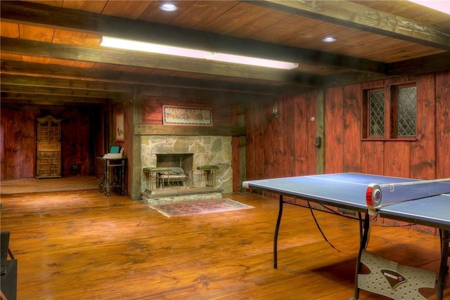 recreation room with beam ceiling, a stone fireplace, hardwood / wood-style floors, and wood walls