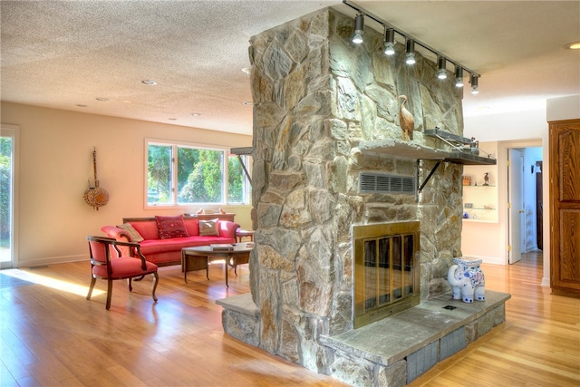 living room featuring light hardwood / wood-style floors, track lighting, a stone fireplace, and a textured ceiling