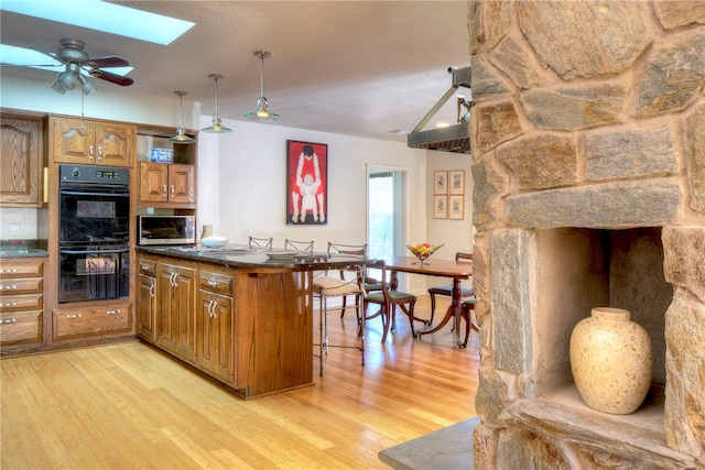 kitchen with ceiling fan, light wood-type flooring, a breakfast bar area, a skylight, and double oven