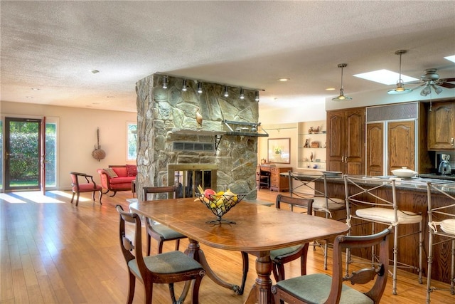 dining room featuring light wood-type flooring, a skylight, a textured ceiling, and a stone fireplace