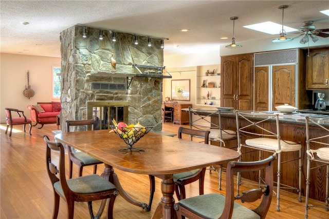 dining room featuring light hardwood / wood-style floors, a skylight, ceiling fan, a fireplace, and a textured ceiling