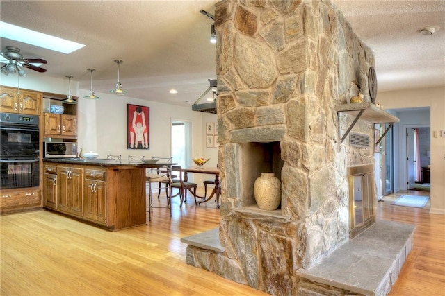 kitchen with a stone fireplace, ceiling fan, a kitchen bar, a textured ceiling, and black double oven