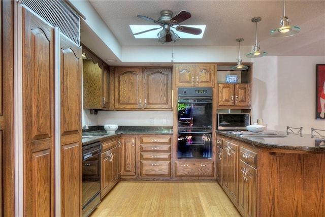 kitchen with decorative light fixtures, a textured ceiling, light hardwood / wood-style floors, a skylight, and black appliances