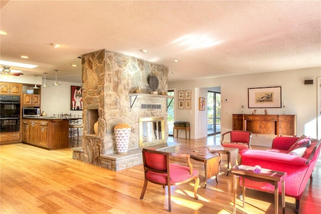 living room with a fireplace, ceiling fan, a textured ceiling, and light hardwood / wood-style flooring