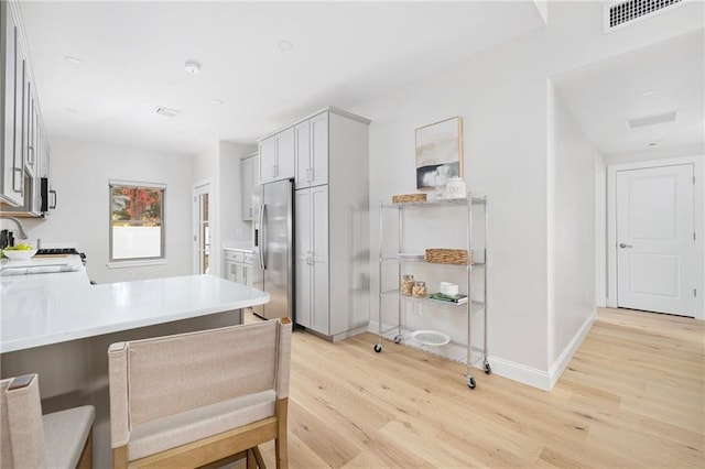 kitchen with light hardwood / wood-style floors, a breakfast bar area, kitchen peninsula, and stainless steel refrigerator with ice dispenser