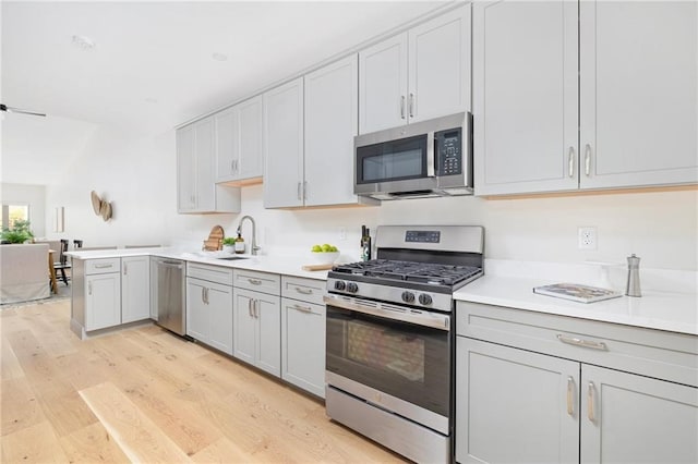 kitchen with kitchen peninsula, stainless steel appliances, sink, and light wood-type flooring