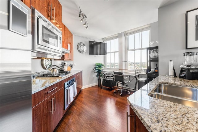 kitchen featuring baseboards, light stone counters, rail lighting, dark wood finished floors, and appliances with stainless steel finishes