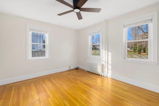 empty room featuring ceiling fan, a healthy amount of sunlight, wood-type flooring, and radiator heating unit