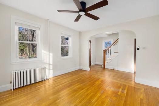 empty room with wood-type flooring, radiator, and ceiling fan