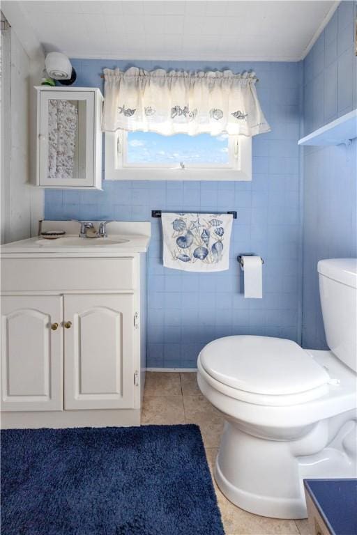 half bathroom with vanity, tile patterned flooring, toilet, and tile walls