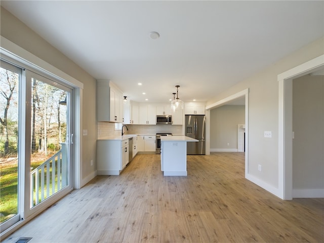 kitchen with white cabinetry, stainless steel appliances, hanging light fixtures, light hardwood / wood-style flooring, and a center island