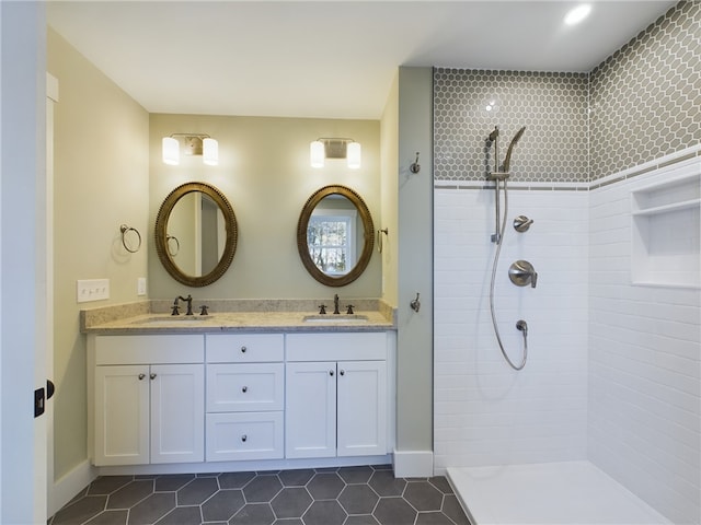 bathroom with tile patterned flooring, a tile shower, and vanity