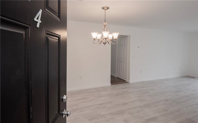 unfurnished room with a chandelier and light wood-type flooring