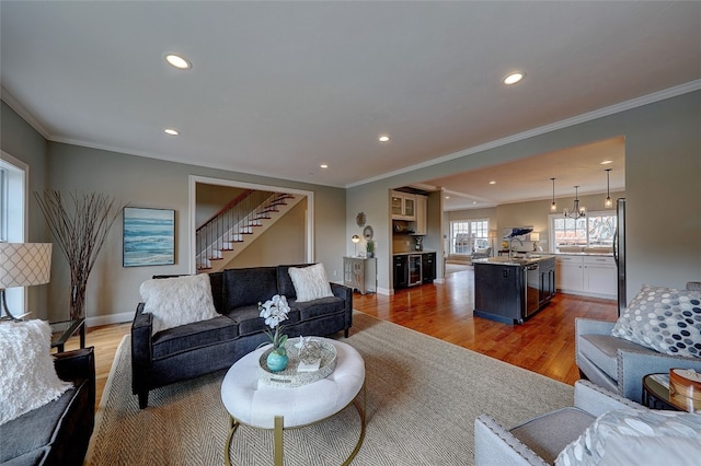 living room with an inviting chandelier, sink, crown molding, and light hardwood / wood-style floors