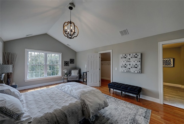 bedroom featuring lofted ceiling, a closet, a walk in closet, light wood-type flooring, and a chandelier