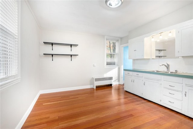 kitchen featuring white cabinetry, sink, radiator, and light hardwood / wood-style flooring