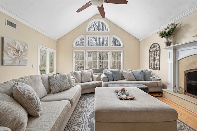 living room with hardwood / wood-style floors, crown molding, a fireplace, high vaulted ceiling, and ceiling fan