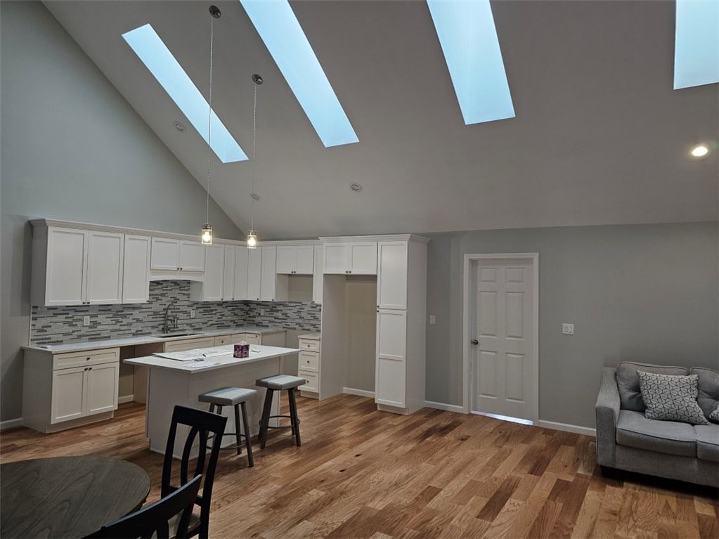 kitchen with light hardwood / wood-style flooring, white cabinets, a center island, and high vaulted ceiling