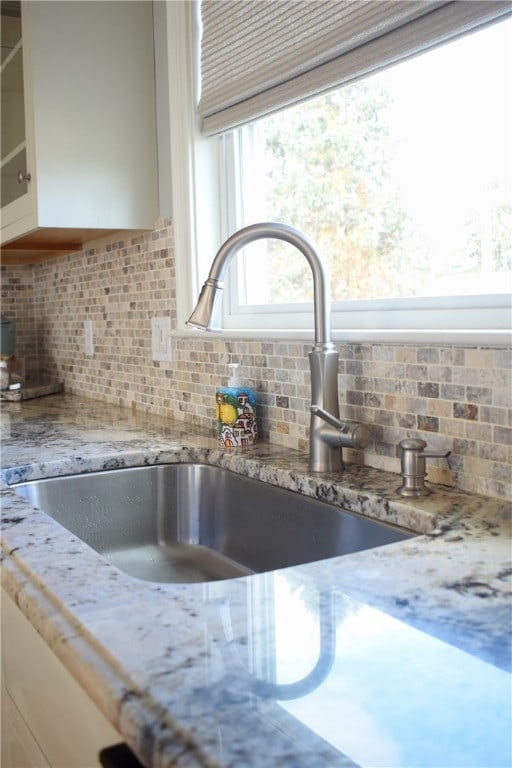 room details with light stone countertops, decorative backsplash, and sink