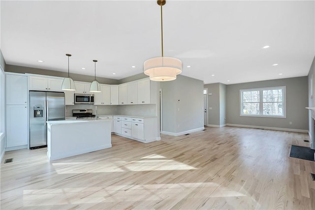 kitchen with white cabinetry, appliances with stainless steel finishes, hanging light fixtures, light hardwood / wood-style flooring, and a center island