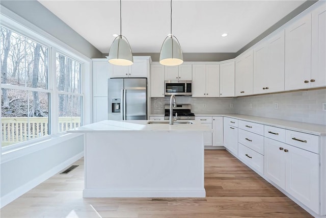 kitchen featuring stainless steel appliances, a kitchen island with sink, hanging light fixtures, white cabinets, and sink