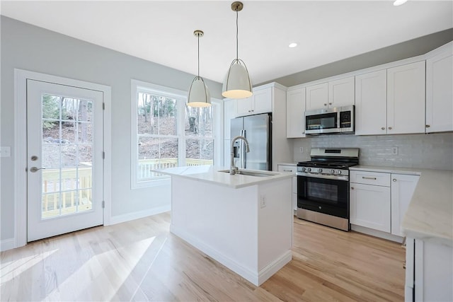 kitchen featuring white cabinetry, stainless steel appliances, decorative backsplash, hanging light fixtures, and a center island with sink