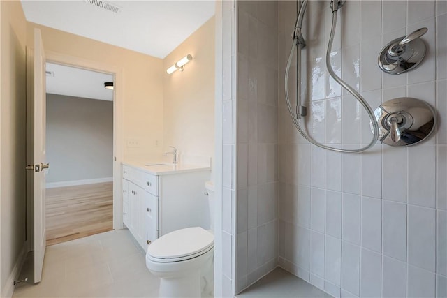 bathroom with toilet, vanity, a tile shower, and tile patterned flooring