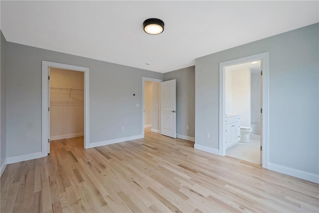 unfurnished bedroom featuring a spacious closet, connected bathroom, a closet, and light wood-type flooring