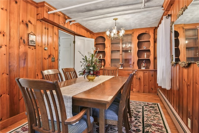 dining area with wood walls, a textured ceiling, baseboard heating, hardwood / wood-style flooring, and an inviting chandelier