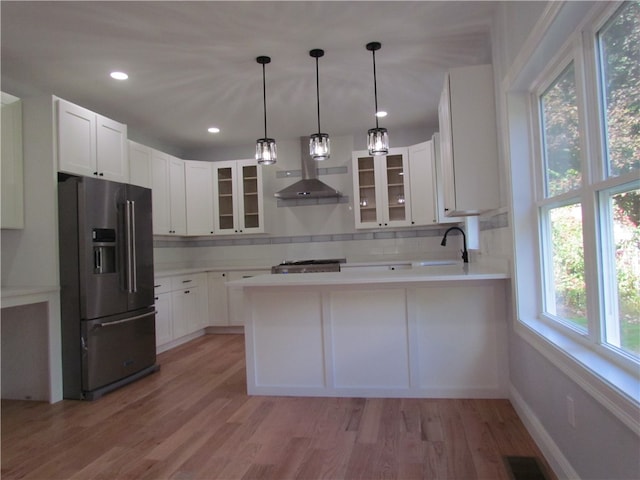 kitchen featuring wall chimney range hood, white cabinetry, light hardwood / wood-style floors, decorative light fixtures, and stainless steel fridge with ice dispenser