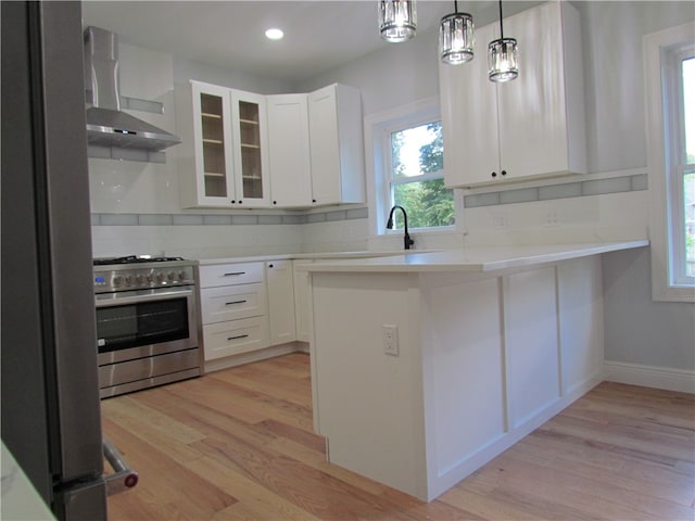 kitchen featuring wall chimney range hood, appliances with stainless steel finishes, white cabinets, decorative backsplash, and light hardwood / wood-style flooring