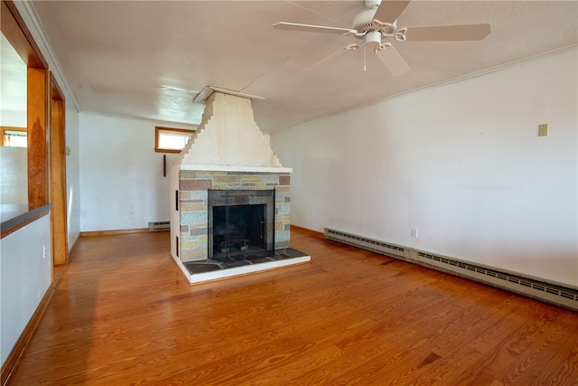 unfurnished living room featuring a baseboard heating unit, hardwood / wood-style floors, ceiling fan, a fireplace, and crown molding