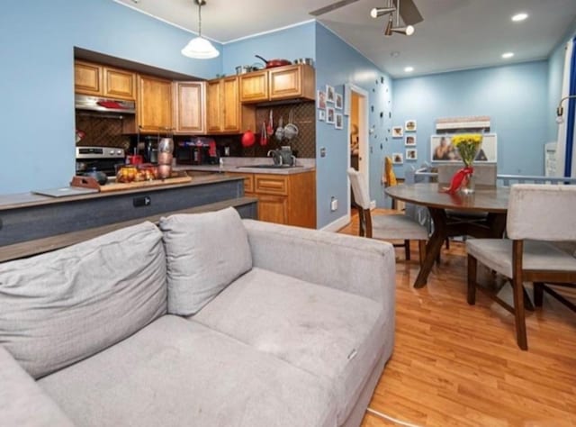 kitchen with light wood-type flooring, pendant lighting, sink, decorative backsplash, and stainless steel range oven