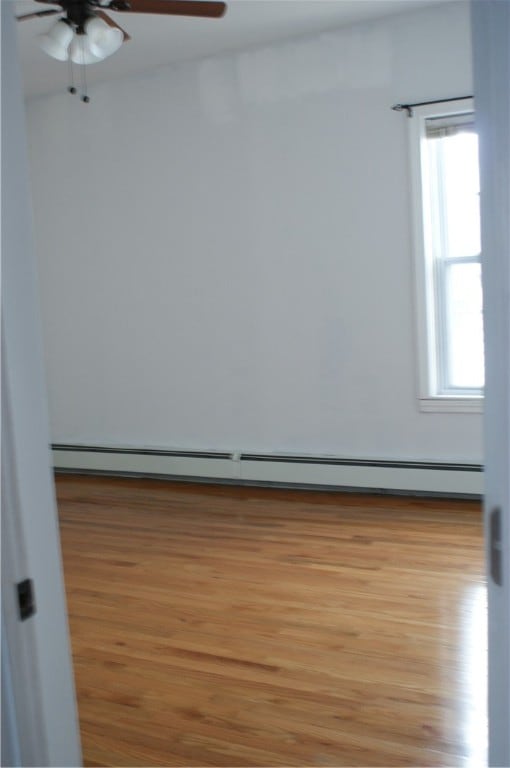 spare room with baseboard heating, light wood-type flooring, and ceiling fan