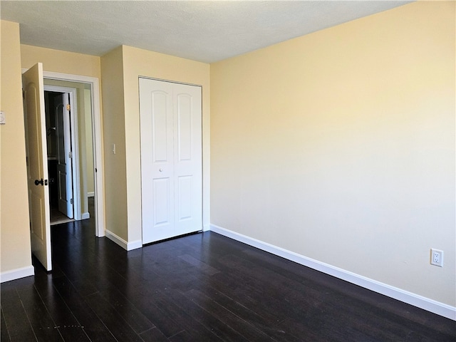 unfurnished bedroom featuring a textured ceiling, dark hardwood / wood-style flooring, and a closet